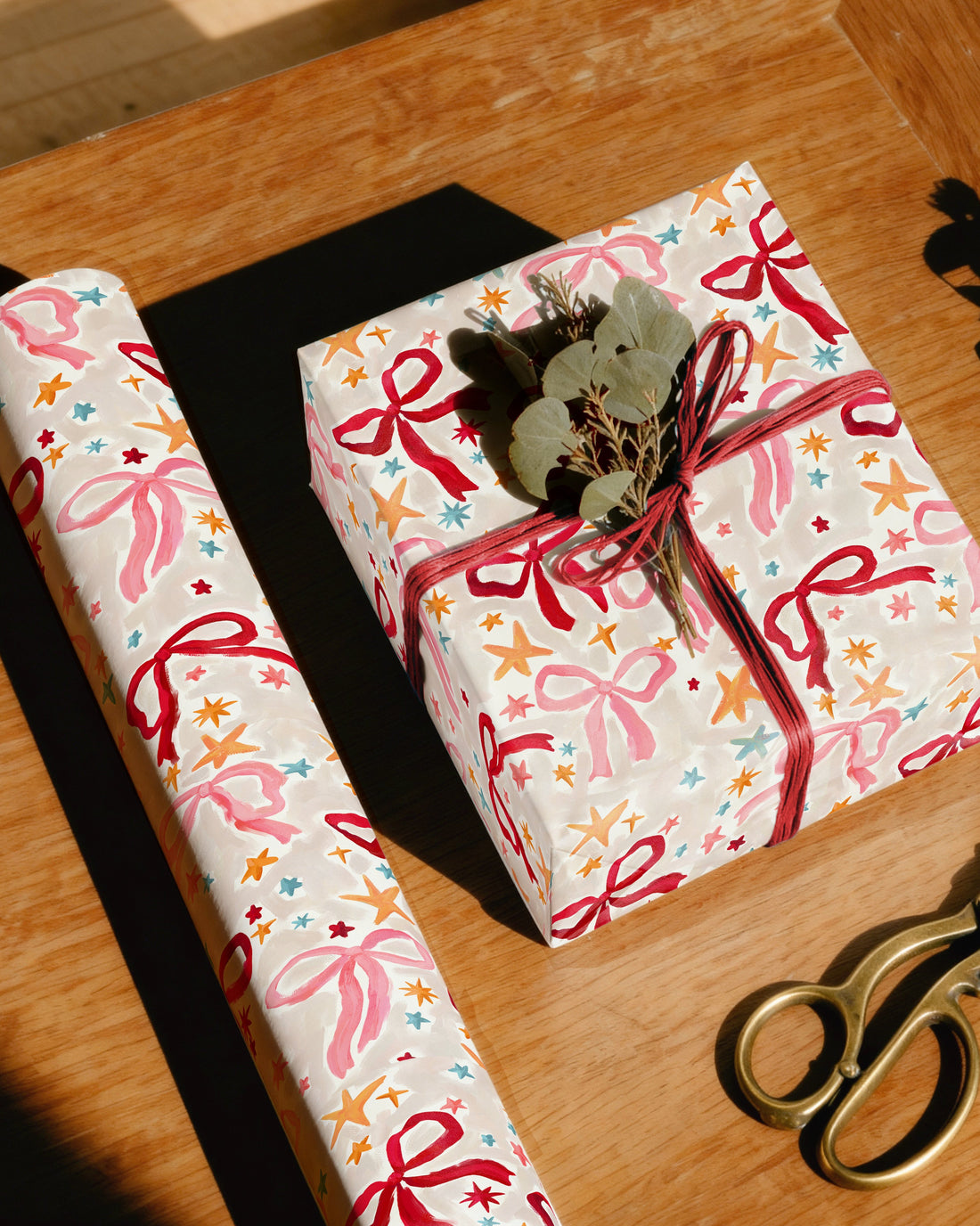 Gift wrapped in colorful paper with ribbons on a wooden table, accompanied by scissors and extra wrapping paper.